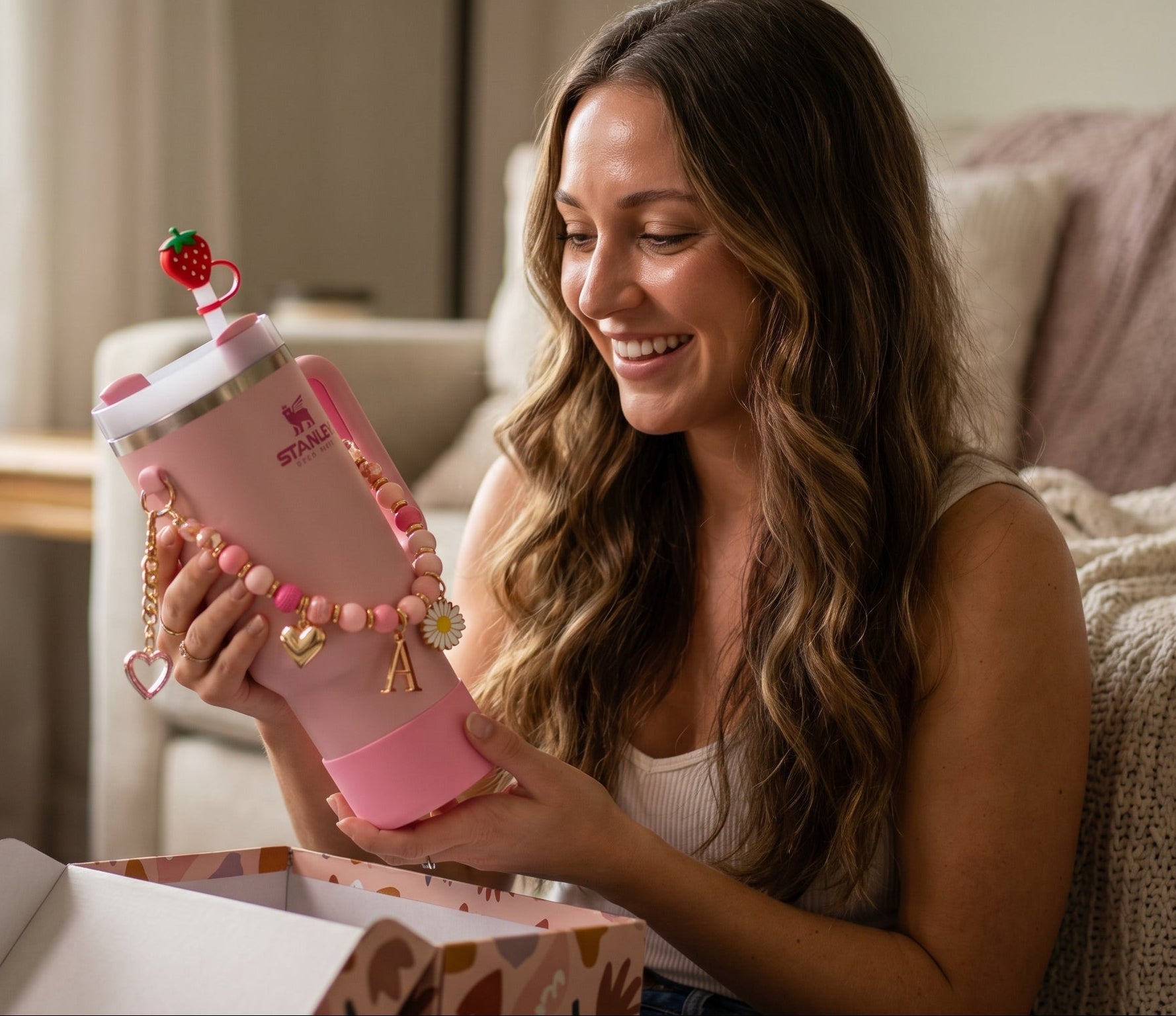 Woman holding a pink phone case with decorative elements in a cozy living room.